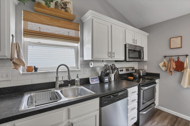840 Gulliver Dr, Columbus, OH 43207 - kitchen featuring appliances with stainless steel finishes, vaulted ceiling, backsplash, dark countertops, and white cabinets