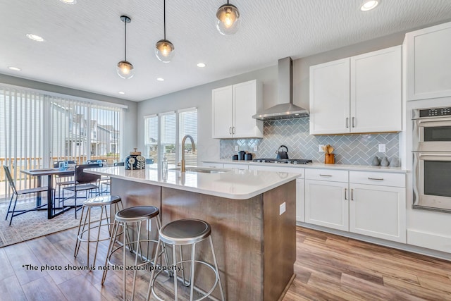 266 Willow Way, Newark, OH 43055 - kitchen with wall chimney exhaust hood, a sink, light wood-style floors, a breakfast bar, and light countertops