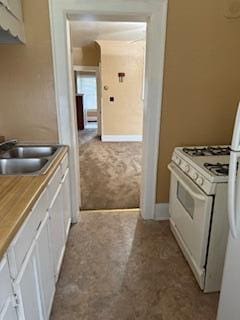 865 E Whittier St, Columbus, OH 43206 - kitchen with white range with gas stovetop, a sink, carpet, white cabinets, and baseboards