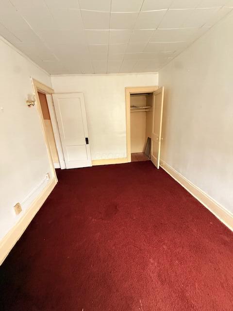 869 E Whittier St, Columbus, OH 43206 - unfurnished bedroom with baseboards, dark colored carpet, and a closet
