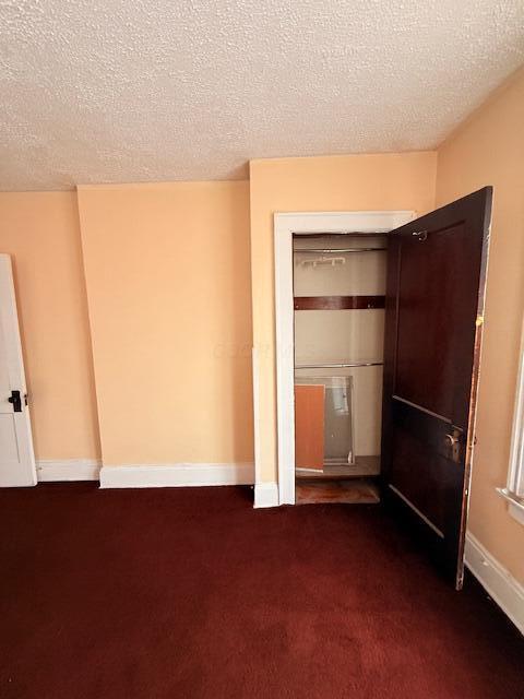 869 E Whittier St, Columbus, OH 43206 - unfurnished bedroom with dark carpet, a textured ceiling, baseboards, and a closet