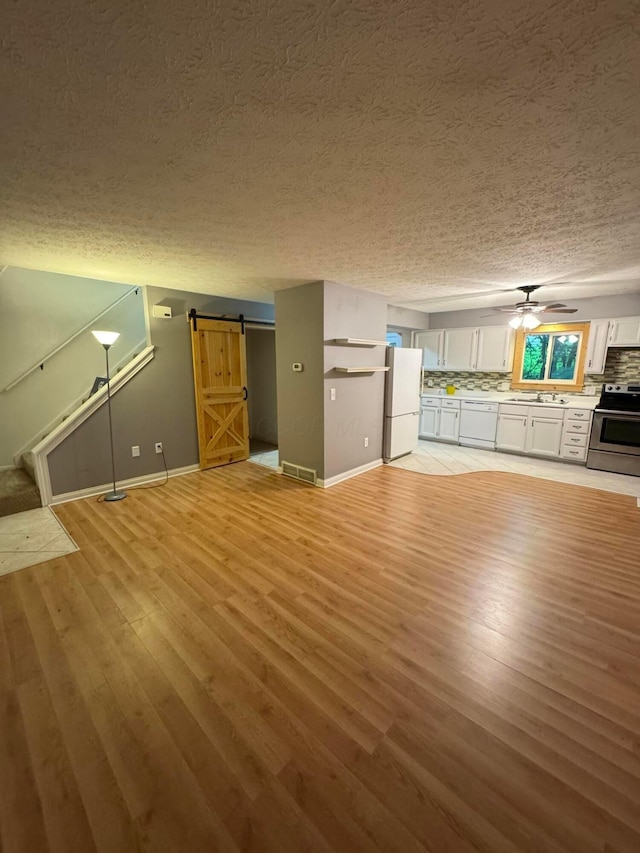 1442 Londondale Unit 3-3, Newark, OH 43055 - unfurnished living room with a textured ceiling, light wood-style flooring, a barn door, baseboards, and a ceiling fan