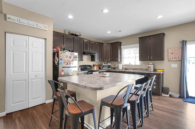 1598 Metcalfe Ave, Obetz, OH 43207 - kitchen with black appliances, under cabinet range hood, dark brown cabinets, a sink, and a breakfast bar