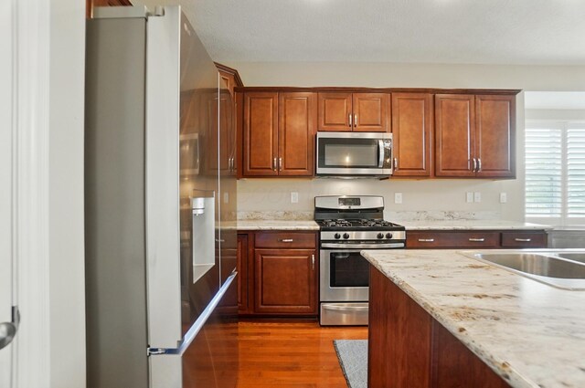 6368 Casado Dr, Columbus, OH 43213 - kitchen featuring stainless steel appliances, wood finished floors, brown cabinets, and light stone counters