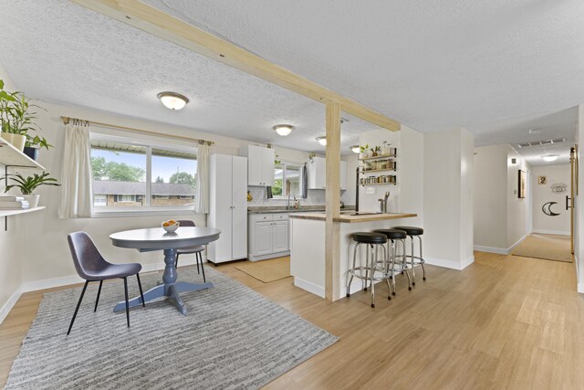 6576 Creon Dr, Reynoldsburg, OH 43068 - kitchen with light wood finished floors, a breakfast bar, a peninsula, a textured ceiling, and baseboards
