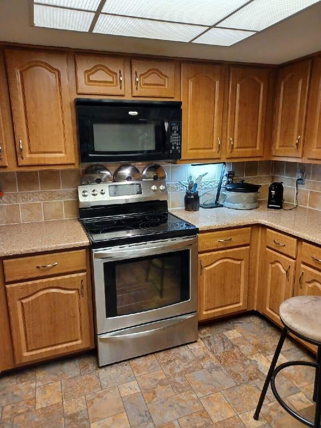 5935 N High St Unit 202, Worthington, OH 43085 - kitchen featuring black microwave, stainless steel electric stove, stone tile flooring, backsplash, and brown cabinets