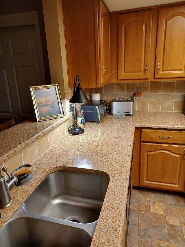 5935 N High St Unit 202, Worthington, OH 43085 - kitchen featuring a sink, backsplash, brown cabinets, and light stone finish floors