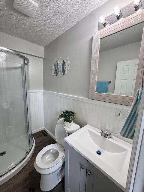 1729 E 17th Ave, Columbus, OH 43219 - bathroom featuring wood finished floors, toilet, a wainscoted wall, a stall shower, and vanity