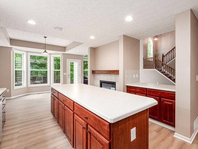 7034 Kellogg Dr, Powell, OH 43065 - kitchen with light wood-style flooring, a center island, a fireplace, light countertops, and pendant lighting