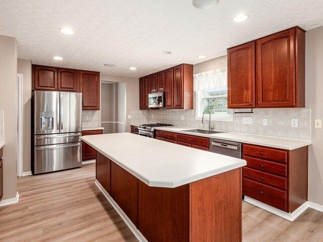 7034 Kellogg Dr, Powell, OH 43065 - kitchen featuring stainless steel appliances, a sink, a textured ceiling, light wood finished floors, and a center island