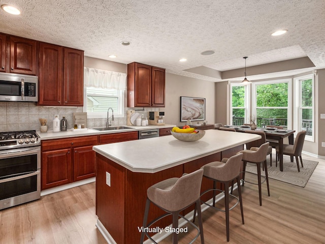 7034 Kellogg Dr, Powell, OH 43065 - kitchen featuring appliances with stainless steel finishes, a sink, a kitchen breakfast bar, light wood-style flooring, and light countertops