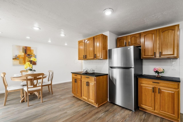 3944 Ardath Rd, Columbus, OH 43228 - kitchen with freestanding refrigerator, brown cabinetry, dark countertops, dark wood-style floors, and a textured ceiling