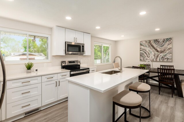 2142 Balford Sq W, Columbus, OH 43232 - kitchen featuring appliances with stainless steel finishes, light wood-style floors, a center island with sink, recessed lighting, and white cabinetry