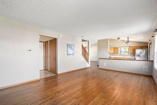 4686 Gilman Rd, Columbus, OH 43228 - unfurnished living room with vaulted ceiling, wood finished floors, stairs, a textured ceiling, and baseboards