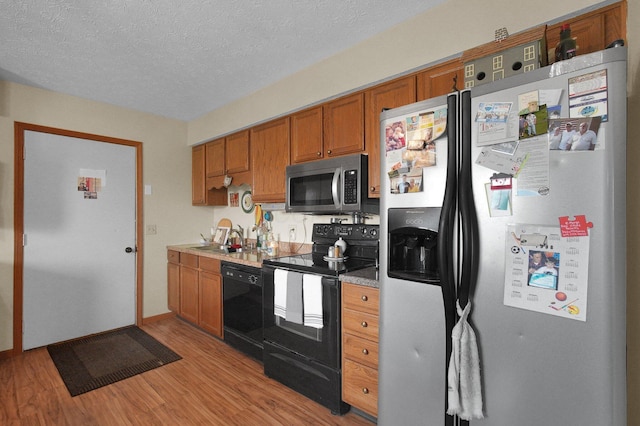 452 Samantha Cir Unit 10, London, OH 43140 - kitchen featuring black appliances, light wood-style flooring, brown cabinets, a sink, and a textured ceiling