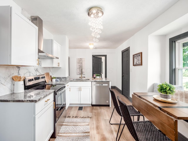 1432 Cordell Ave, Columbus, OH 43211 - kitchen with appliances with stainless steel finishes, wall chimney exhaust hood, a peninsula, light wood-style flooring, and a chandelier