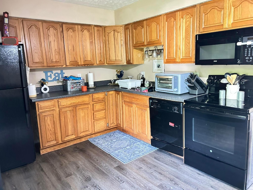 375 Darby Ct, Galloway, OH 43119 - kitchen with black appliances, dark wood-style floors, brown cabinetry, a textured ceiling, and dark countertops