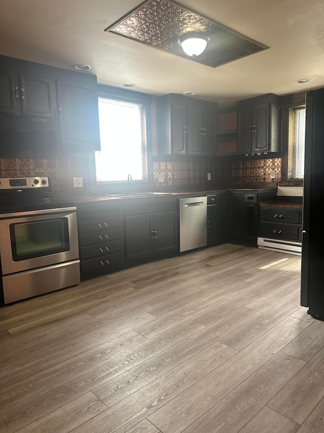 287 W Columbus St, Mount Sterling, OH 43143 - kitchen with appliances with stainless steel finishes, light wood-type flooring, decorative backsplash, a baseboard heating unit, and dark countertops