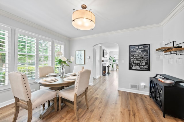 1572 Barrington Rd, Upper Arlington, OH 43221 - dining room featuring arched walkways, light wood-type flooring, crown molding, a warm lit fireplace, and baseboards