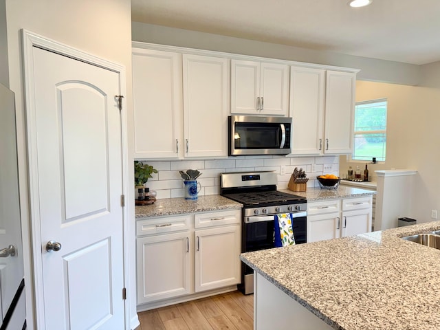3895 Brody Dr, Grove City, OH 43123 - kitchen with appliances with stainless steel finishes, white cabinets, light wood-style floors, tasteful backsplash, and light stone counters