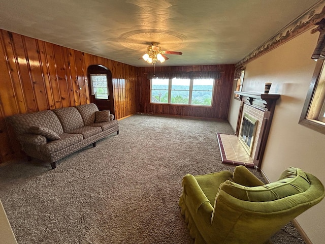 3049 Palace Heights Ln NW, Malta, OH 43758 - carpeted living room featuring wood walls, arched walkways, a ceiling fan, and a fireplace with raised hearth