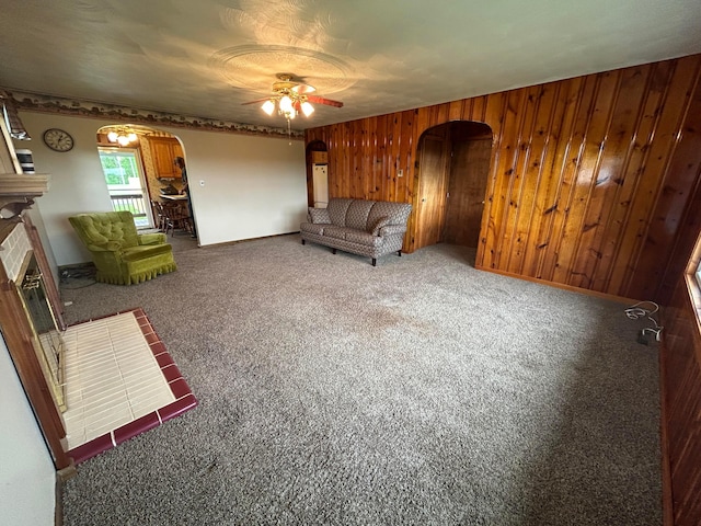 3049 Palace Heights Ln NW, Malta, OH 43758 - unfurnished living room with arched walkways, ceiling fan, wooden walls, carpet floors, and a tiled fireplace