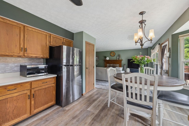 388 Slate Run Dr, Powell, OH 43065 - kitchen with appliances with stainless steel finishes, light wood finished floors, a textured ceiling, brown cabinetry, and backsplash