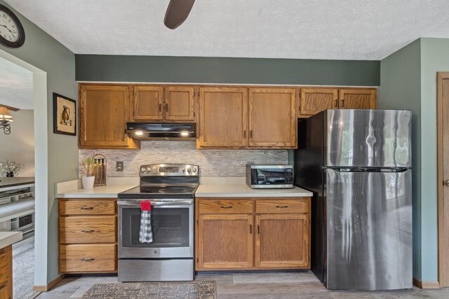 388 Slate Run Dr, Powell, OH 43065 - kitchen with appliances with stainless steel finishes, under cabinet range hood, light countertops, light wood-style flooring, and a textured ceiling