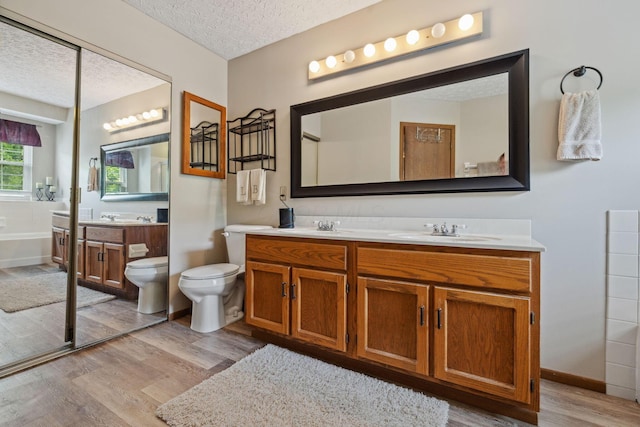 388 Slate Run Dr, Powell, OH 43065 - bathroom featuring wood finished floors, a textured ceiling, double vanity, toilet, and a bath