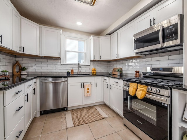 1156 S Champion Ave, Columbus, OH 43206 - kitchen featuring appliances with stainless steel finishes, decorative backsplash, white cabinets, dark countertops, and light tile patterned flooring
