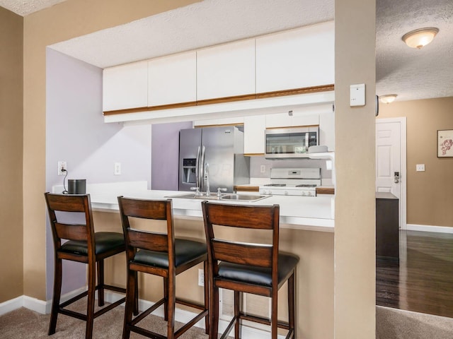 5678 Mango Ln Unit 104A, Hilliard, OH 43026 - kitchen with stainless steel appliances, a textured ceiling, a peninsula, white cabinets, and a breakfast bar