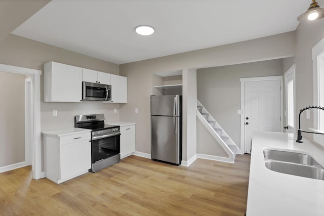 704 N Detroit St, Bellefontaine, OH 43311 - kitchen with appliances with stainless steel finishes, a sink, light wood-style flooring, white cabinetry, and light countertops