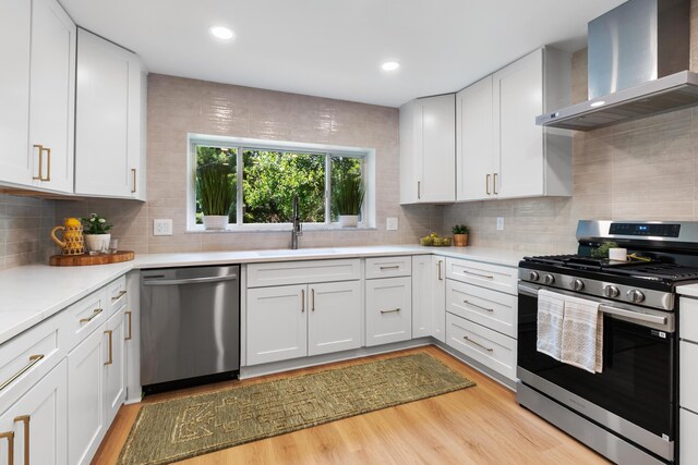 75 S Gould Rd, Columbus, OH 43209 - kitchen with appliances with stainless steel finishes, wall chimney range hood, light countertops, white cabinets, and light wood-style floors