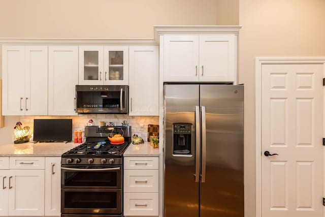 5893 Dunheath Loop, Dublin, OH 43016 - kitchen with appliances with stainless steel finishes, white cabinetry, backsplash, glass insert cabinets, and light stone countertops