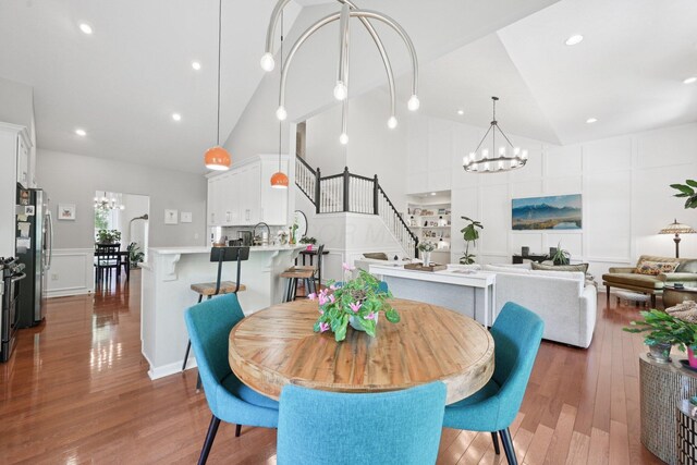 5893 Dunheath Loop, Dublin, OH 43016 - dining space with a chandelier, high vaulted ceiling, a decorative wall, stairway, and wood finished floors