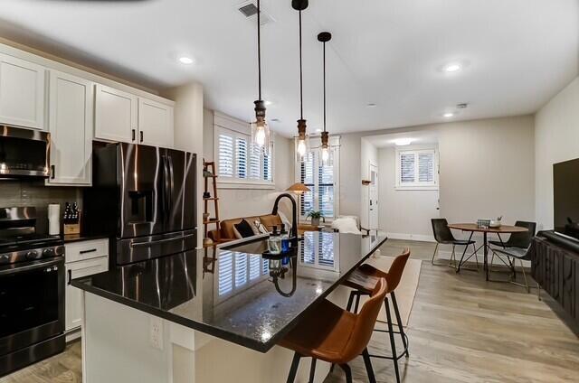 1301 Highland St, Columbus, OH 43201 - kitchen featuring appliances with stainless steel finishes, a center island with sink, white cabinets, a breakfast bar area, and decorative light fixtures