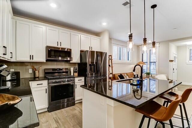 1301 Highland St, Columbus, OH 43201 - kitchen with stainless steel appliances, light wood-style flooring, white cabinetry, a kitchen breakfast bar, and tasteful backsplash