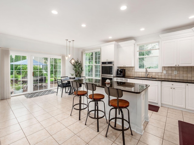 6165 Avocet Ct, Dublin, OH 43017 - kitchen with double oven, light tile patterned floors, backsplash, a center island, and crown molding