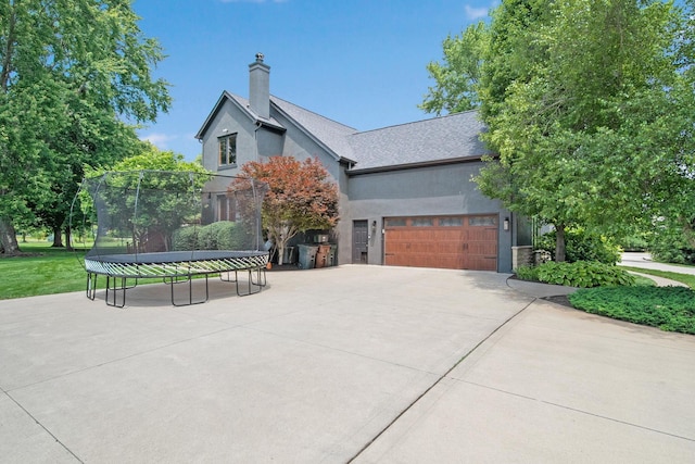 2946 Lewis Center Rd, Lewis Center, OH 43035 - view of property exterior featuring a trampoline, stucco siding, a garage, concrete driveway, and a chimney