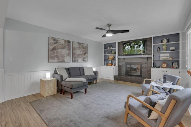 13680 Nantucket Ave NW, Pickerington, OH 43147 - living room with wood finished floors, a ceiling fan, a brick fireplace, built in features, and a wainscoted wall