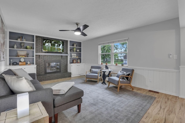 13680 Nantucket Ave NW, Pickerington, OH 43147 - living room with wood finished floors, built in features, a ceiling fan, a fireplace, and wainscoting