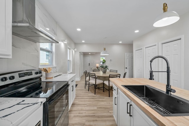 591 S 22nd St, Columbus, OH 43205 - kitchen with stainless steel electric range, butcher block countertops, wall chimney exhaust hood, light wood-style floors, and white cabinetry