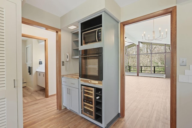 220 Hardy Way, Worthington, OH 43085 - bar area featuring wine cooler, black oven, light wood-style flooring, a chandelier, and baseboards