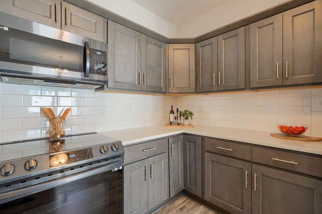 1957 Cumberland St, Newark, OH 43055 - kitchen featuring stainless steel appliances, light countertops, light wood finished floors, decorative backsplash, and a textured ceiling