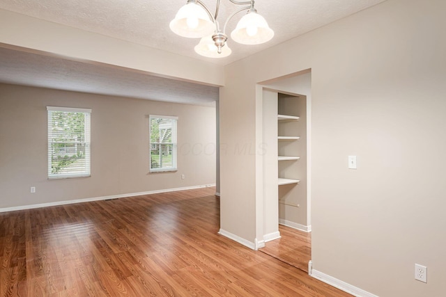 8800 Greenburg Dr, Powell, OH 43065 - empty room featuring a chandelier, light wood finished floors, baseboards, and a textured ceiling