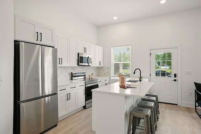 92 E Innis Ave, Columbus, OH 43207 - kitchen featuring stainless steel appliances, light wood finished floors, decorative backsplash, a kitchen island with sink, and recessed lighting