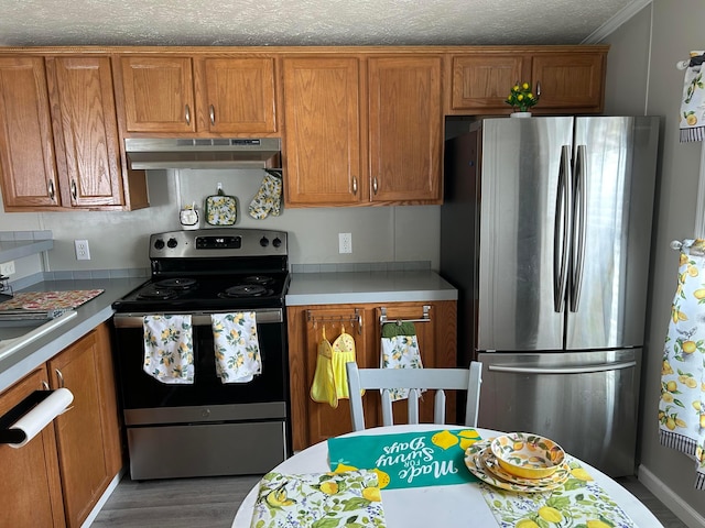 5019 N High St Unit 97, Columbus, OH 43214 - kitchen featuring appliances with stainless steel finishes, under cabinet range hood, brown cabinetry, light countertops, and wood finished floors