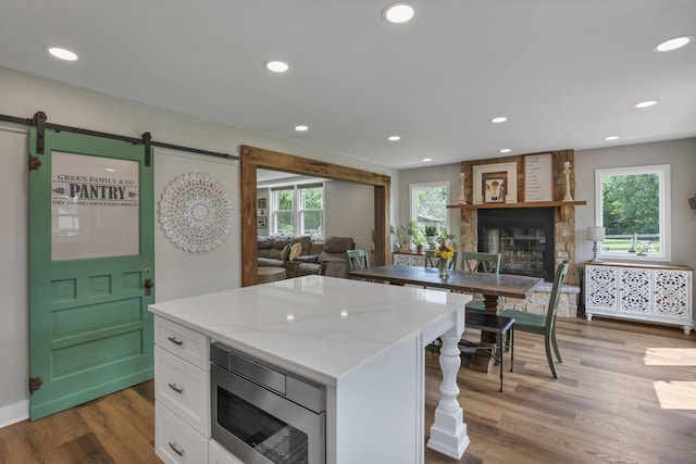 1859 State Route 257 N, Ostrander, OH 43061 - kitchen featuring stainless steel microwave, white cabinetry, a barn door, a stone fireplace, and wood finished floors