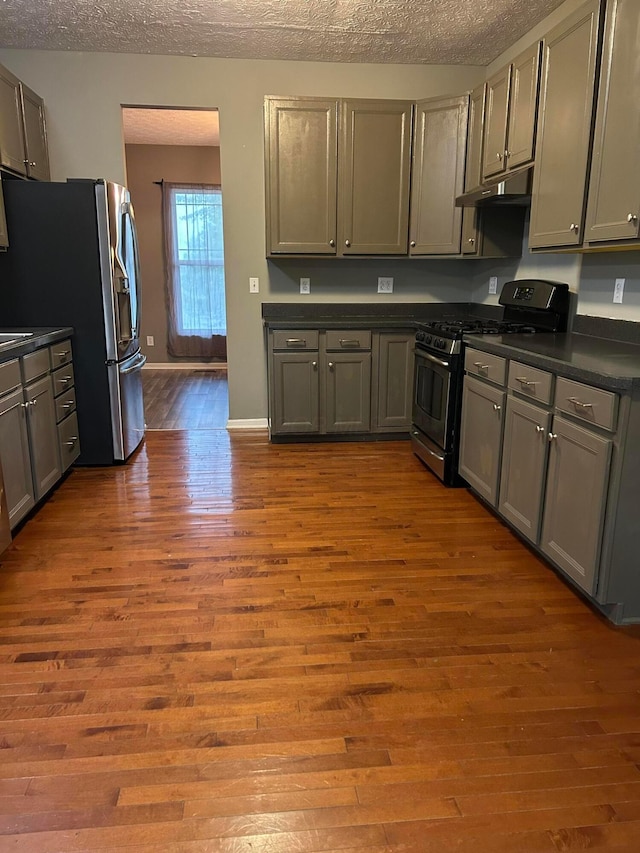 1021 Taylor Glen Blvd E, Pataskala, OH 43062 - kitchen featuring gas range oven, under cabinet range hood, dark countertops, dark wood-type flooring, and stainless steel fridge