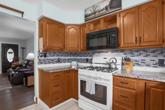 568 Swackhammer Rd, Circleville, OH 43113 - kitchen with black microwave, white gas range, brown cabinetry, and tasteful backsplash